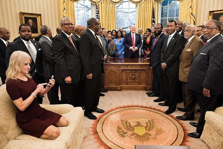 Ms Kellyanne Conway checks her phone soon after kneeling down on an Oval Office couch to take a photo of Mr Donald Trump and leaders of historically black universities and colleges in the US.