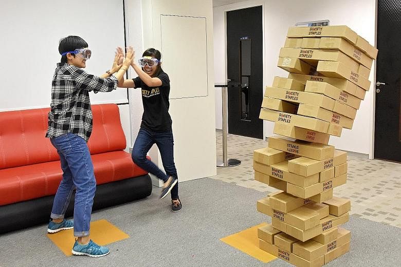 Events management executive Tay Puay Shan (left) and co-founder of Society Staples Debra Lam playing Giant Jenga with special goggles that simulate different kinds of visual disabilities.