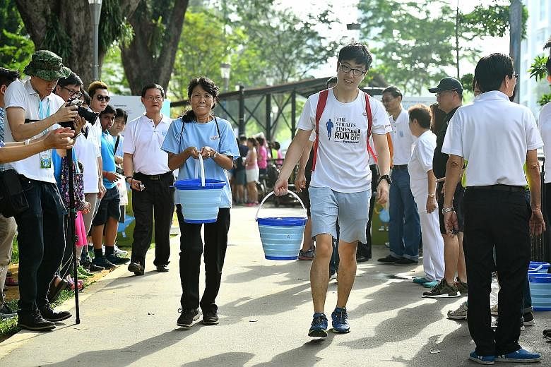 Housewife Seah Wah Kiang, 59, and finance associate Yu Yang, 30, carrying recycled water in the "Race for Water", one of the activities at an event yesterday to celebrate Singapore World Water Day. It was held next to the Geylang River.