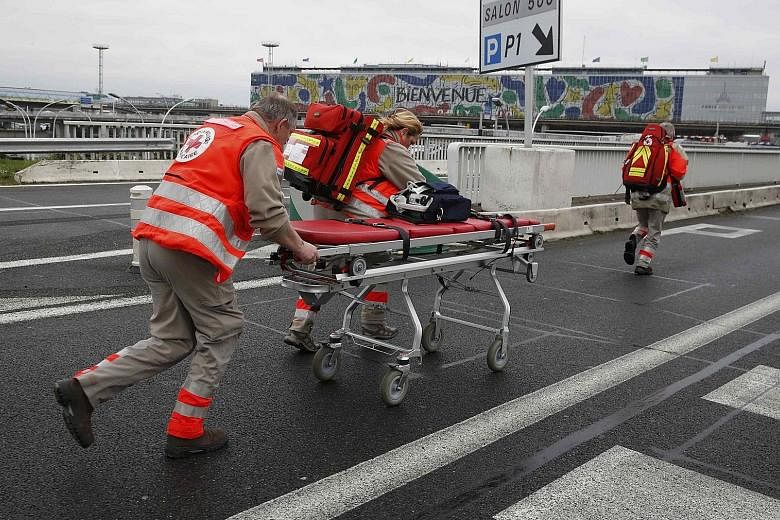 From top: A woman being kept warm under a rescue blanket was among the thousands who were forced to evacuate the Orly-Sud terminal after the shoot-out yesterday. Emergency workers rushed in to provide medical assistance, even as stranded passengers w