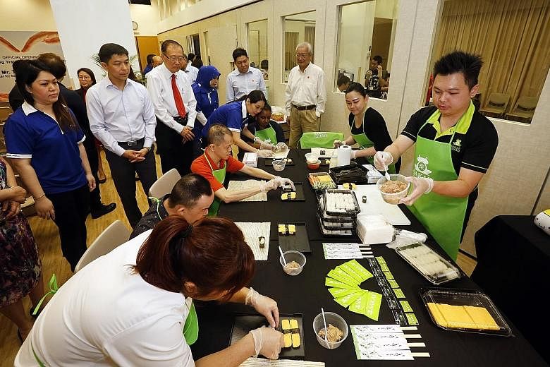 Minister Tan Chuan-Jin and Minds president Jeffrey Tan (with red tie) look on as clients with intellectual disabilities learn sushi-making. Sakae Sushi has committed to training users of the Minds centre.