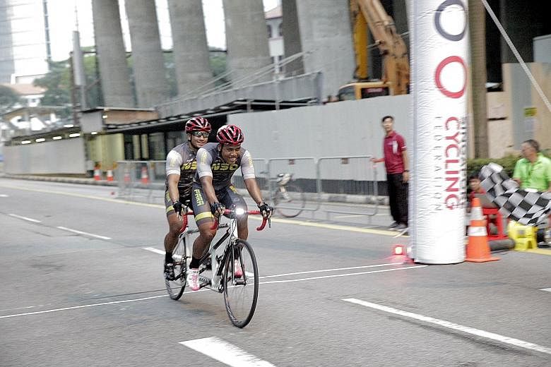 Visually-impaired Afiq Afify Rizan (rear seat) and his able-bodied partner Khairul Adha Rasol crossing the finish line yesterday to win the National Para Cycling Road Championship and International Invitational. The event, held on Cecil Street and Ro