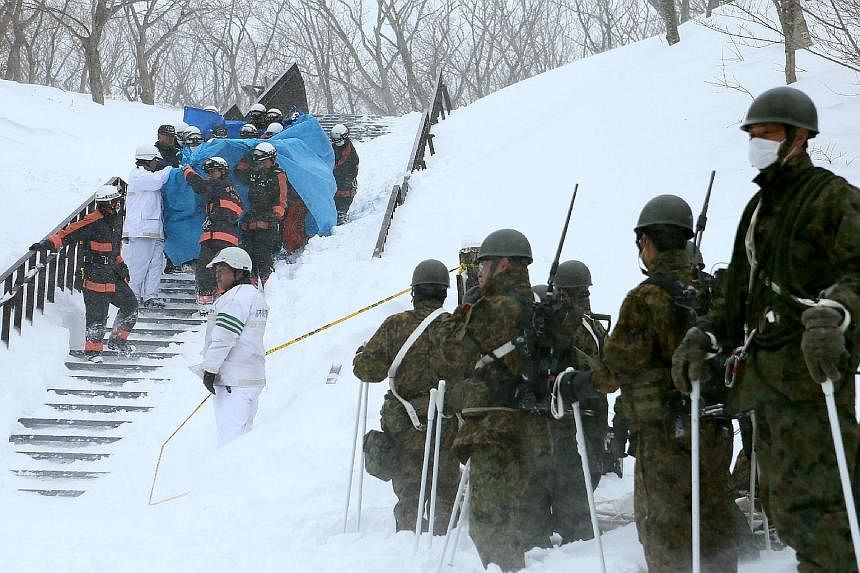Firefighters carrying a survivor from the site of an avalanche in Nasu town, Tochigi prefecture, yesterday. Self Defence Force personnel were also present. Eight teenagers from a high school mountaineering club died, while dozens of other students an