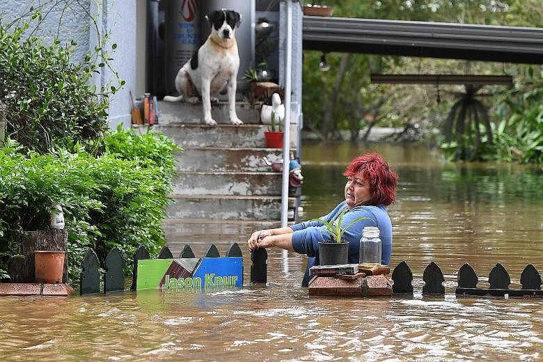 A woman attempting to gain access to her home as her dog looks on in Lismore in New South Wales as floodwaters swirl around her. The Lismore region has been declared a natural disaster zone. An aerial view (right) of houses in Lismore hit by extensiv