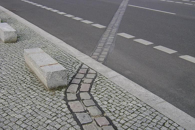 Cobblestone markers that indicate where the Berlin Wall once stood. A writer suggests that something similar be done in Singapore to show where the original shoreline was before land reclamation.