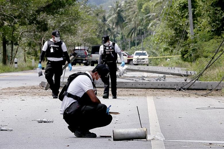 Thai forensic police officers inspecting bomb-damaged power poles at a blast scene in the southern province of Pattani yesterday. Arson and bomb attacks caused widespread blackouts in four southern provinces.