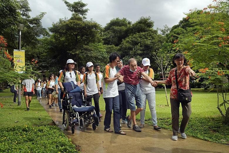 Madam Rebecca Wong, 65, leading the way to encourage her husband, Mr Tay Yam Hwee, 71, at a mass walk yesterday at the Toa Payoh Town Park, during the Parkinson Society Singapore's annual "Move to Beat Parkinson" Day. The event, now in its fourth yea