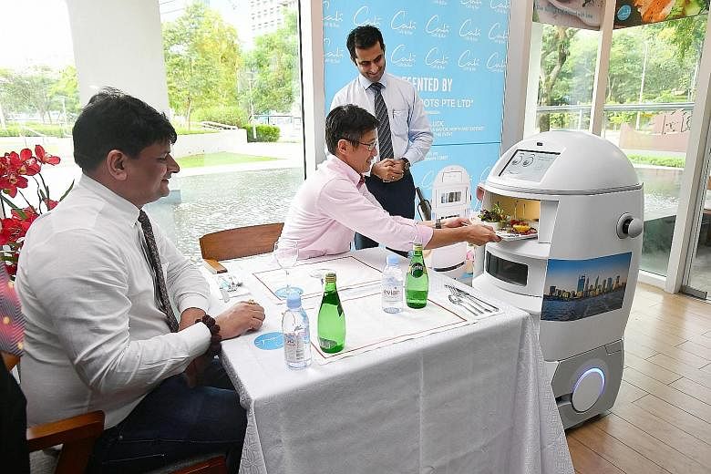 At the Park Avenue Rochester Hotel, Minister of State for Manpower Teo Ser Luck takes a dish out of a food service robot, developed by food and beverage solutions provider Happy Roots. With Mr Teo are the firm's founder and CEO Neelendra Jain (left),