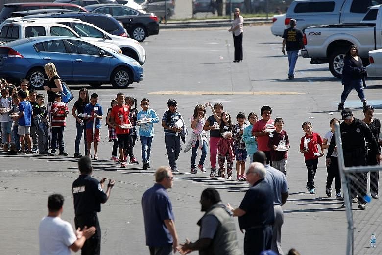 Pupils who were evacuated after a school shooting in San Bernardino, California, walking past well-wishers to be reunited with their waiting parents on Monday. A teacher and a pupil died when the teacher's estranged husband walked into their class an