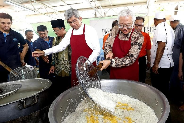Minister-in-charge of Muslim Affairs Yaacob Ibrahim helping President Tony Tan Keng Yam add finishing touches to a pot of briyani at the President's Challenge Charity Briyani, his last one as President.