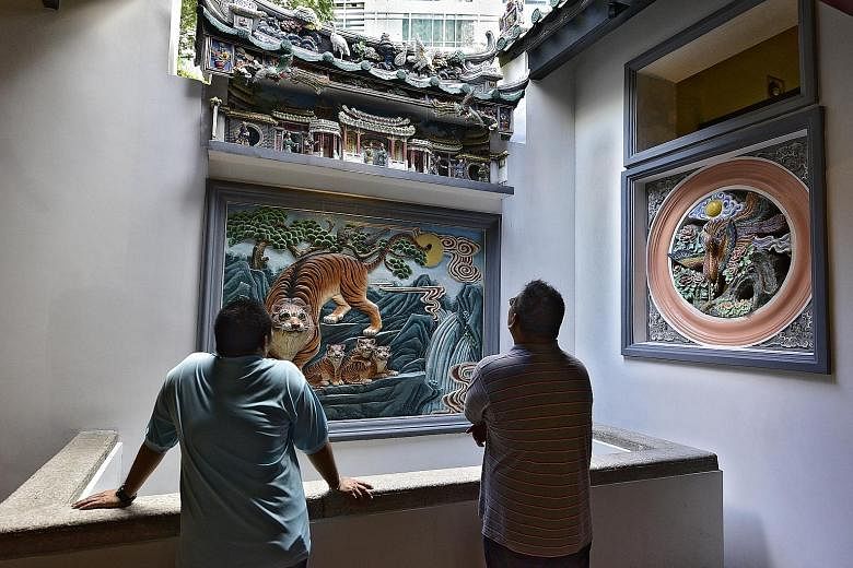Left: A devotee lights joss sticks outside the right hall. Incense urns were moved outdoors to prevent smoke damage to historic carvings inside. Right: Temple caretakers admire a porcelain carving of a tiger and its cubs in the right hall, said to re