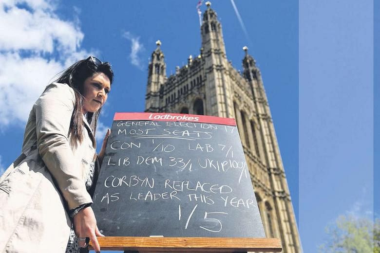  A Ladbrokes betting company staff member holding a sign showing the latest general election odds outside Parliament in London on Tuesday. The Prime Minister could see her majority increase by at least 100 seats at the polls as three MPs from the deeply d