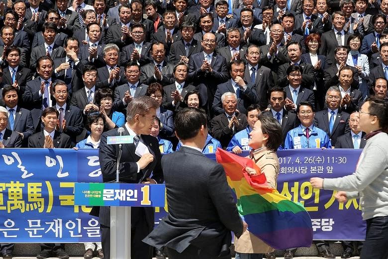 Civic activists with a rainbow flag, known as the "gay pride" flag, protesting to presidential front runner Moon Jae In over his stance against homosexuality, as he campaigned in front of the National Assembly in Seoul, South Korea, yesterday.