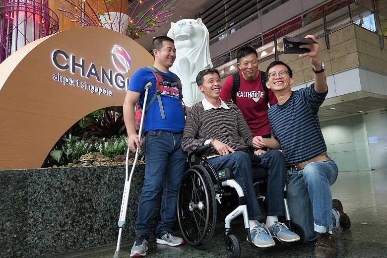 Mr Meng breaking into a rare smile while taking a wefie with manager Jeffrey Chua (holding camera) and volunteers Zhang Xihong (left) and Wang Qingguo at Changi Airport Terminal 2 Mr Meng being helped by a stewardess into his wheelchair upon arrival 