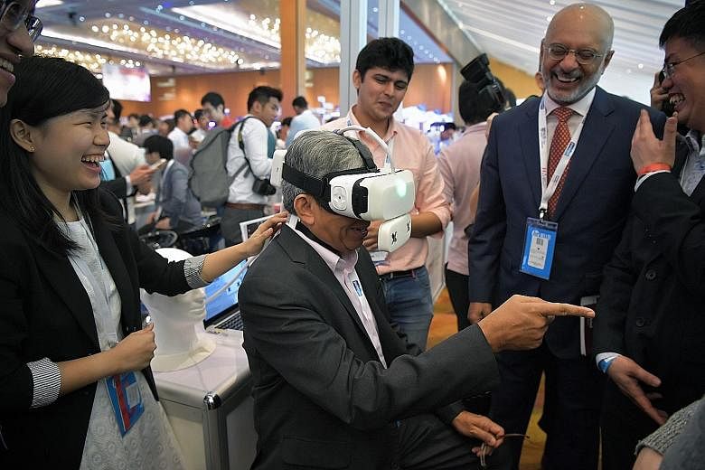 Dr Yaacob Ibrahim trying out the Ambiotherm, a virtual reality headset accessory developed by NUS that simulates ambient temperatures and wind conditions, at the innovation conference yesterday. With him was DBS Group chief executive Piyush Gupta (ri