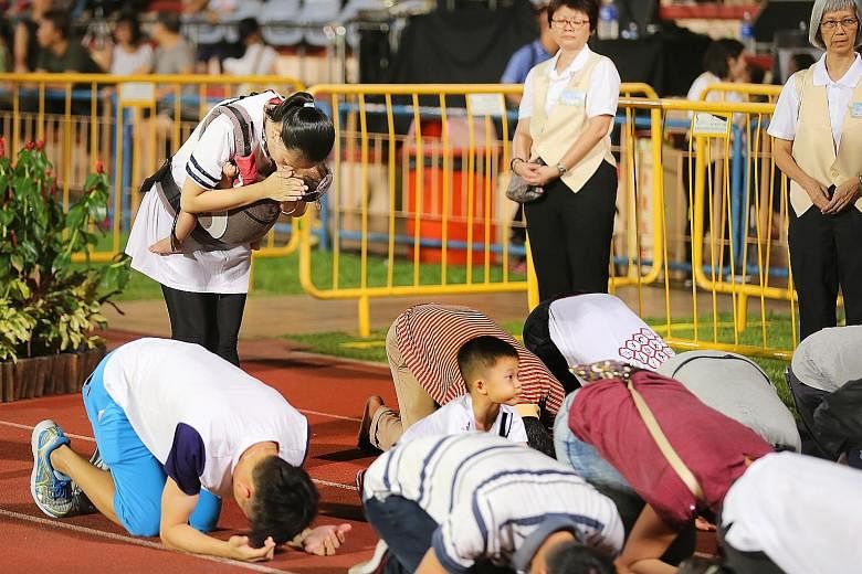 Above: Devotees lined Hougang Stadium's running track as they took three steps, knelt and bowed deeply with their foreheads touching the ground. Left: Ms Jaime Liao (standing), 32, and her son Lexuan (looking up), five, at the Vesak Day event. Minist