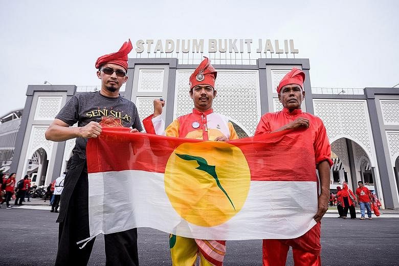 Umno members from Kulim, Kedah, holding up the party flag yesterday outside the Bukit Jalil National Stadium, which was filled with more than 120,000 people including members of the young women's wing, Puteri Umno (above, right), who gathered at the 