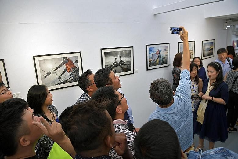 Visitors taking a wefie at an exhibition showcasing frame prints from the photo book, By Day & By Night: Missions Of RSS Sovereignty, which depicts the daily lives of the last crew of the Singapore navy patrol vessel.