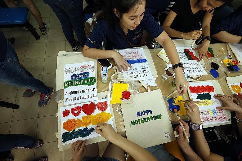 Marina Bay Sands (MBS) staff painting tote bags for underprivileged mothers at the Singapore Association for the Deaf (SADeaf) yesterday, ahead of Mother's Day today. MBS has partnered SADeaf since 2013. Ms Grace Phua with her parents Angela Lee and 