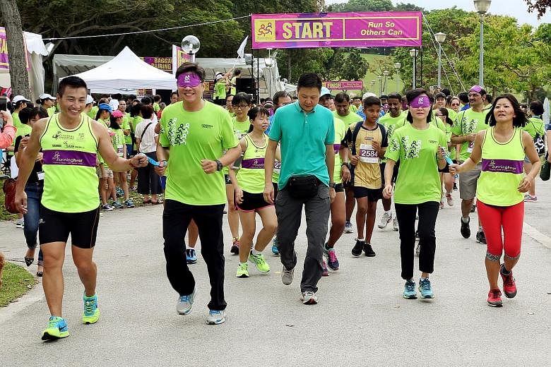 Minister for Education (Schools) Ng Chee Meng running blindfolded at yesterday's Runninghour in Bedok Reservoir, guided by group founder John See Toh. Mr Ng and his wife Michelle (right) ran for 1km.