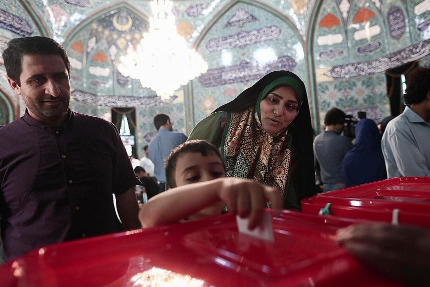 An Iranian boy casting his mother's ballot for the presidential election in Teheran yesterday. People queued in temperatures topping 32 deg C to vote. Shortly before polls were due to close, state television reported that voting was extended by at le