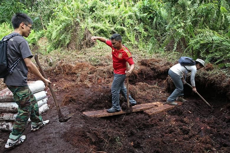 PM.Haze volunteers Iris Ng (front), 25, and Bernice Lau, 36, dig up the peat soil so it can be packed into empty rice sacks to construct the canal block.