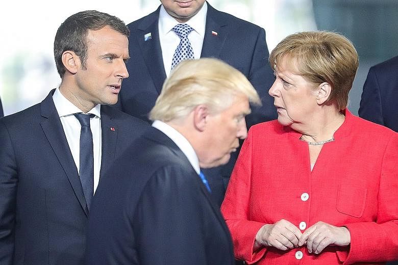 French President Emmanuel Macron (left) talking with German Chancellor Angela Merkel as US President Donald Trump walks by, during a line-up for a group photo at the Nato summit on Thursday.