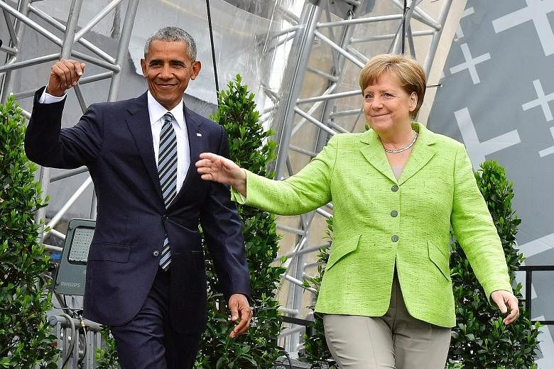 Former US president Barack Obama and German Chancellor Angela Merkel arriving on stage for a forum on democracy held at the Brandenburg Gate in Berlin yesterday. Mr Obama later spent 90 minutes talking about international and US issues without once m