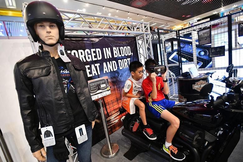 Jayden Koh, 11, trying out the virtual reality technology at the Road Sensibility booth for motorcyclists with his brother Joshua, nine, watching on, at the launch of the Singapore Road Safety Month yesterday. The initiative helps to guide motorcycli