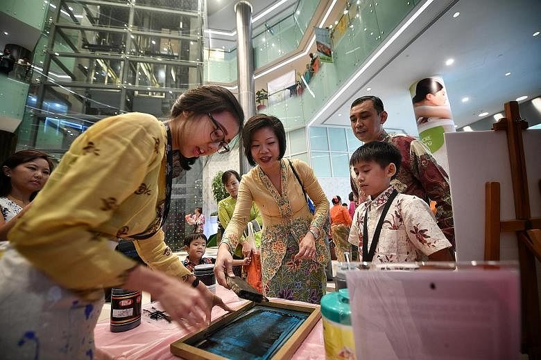 Ms Sim Ann (centre), Senior Minister of State for Culture, Community and Youth, and Trade and Industry, trying out silkscreen printing on a tote bag at the atrium of Claymore Connect mall in Orchard Road yesterday. The activity was part of the Perana