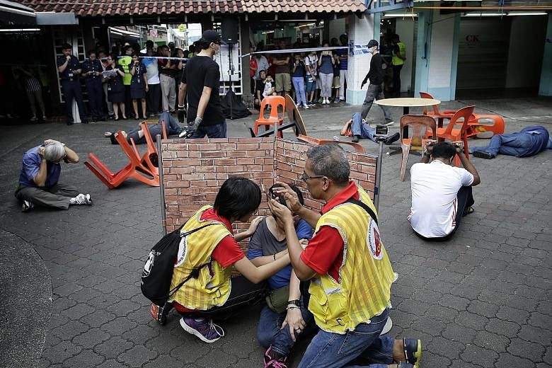 Members of a Community Emergency Response Team helping a "victim" and providing information to the police during a mock terror attack on a coffee shop in Yishun yesterday. Residents also learnt how to help someone having a heart attack and register f