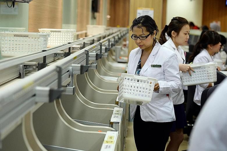 Pharmacy technicians picking up baskets containing medication for patients at the front counter delivered by a new automated system at the Singapore General Hospital's outpatient pharmacy. The system is among new IT innovations in the healthcare sect