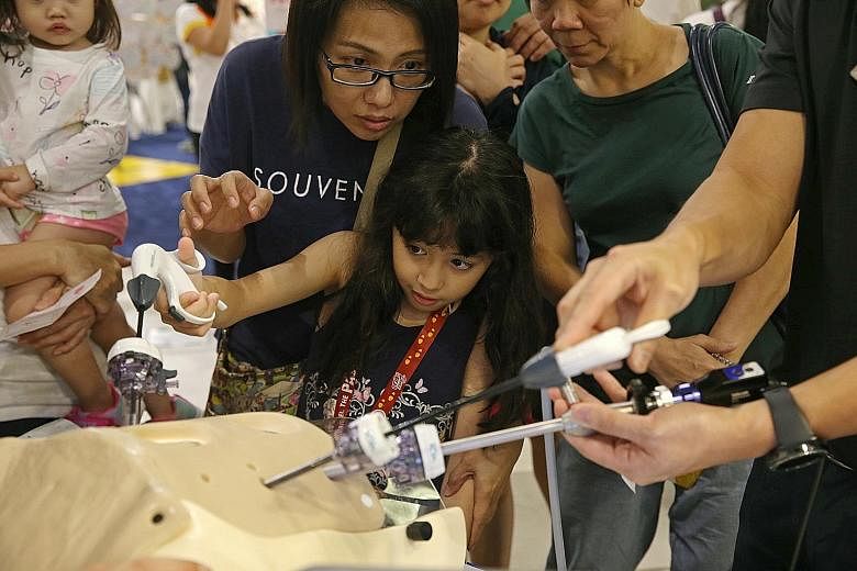 Rachelle Nathalie Mouret, eight, trying the grasper, a device used in the treatment of cancer, with her mother Daphnie Mouret, 43, at the Community Health Fair at Compass One yesterday. The fair is organised by Sengkang Health to raise awareness abou