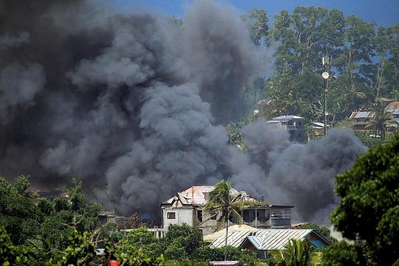 An aircraft launching a rocket during an air strike against the ISIS-linked Maute group in Marawi yesterday. The city (top) has become a battleground as the Philippine military continues its assault on the militants.