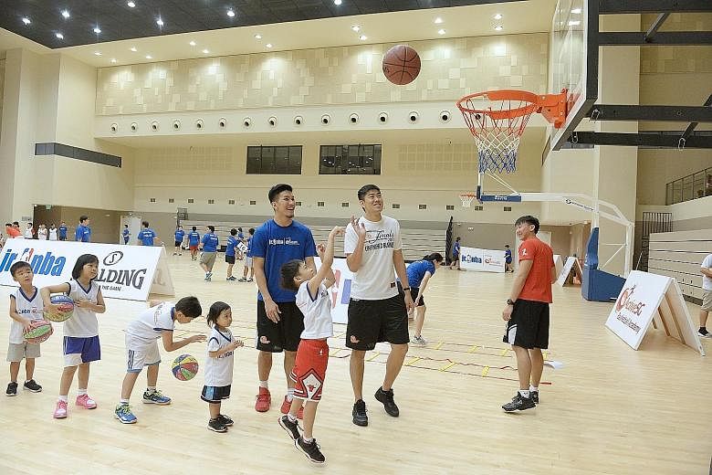 Children lining up to take turns to shoot at yesterday's Jr NBA clinic at Our Tampines Hub sports hall. National player Ng Hanbin (in the blue shirt) was one of the coaches for the day.