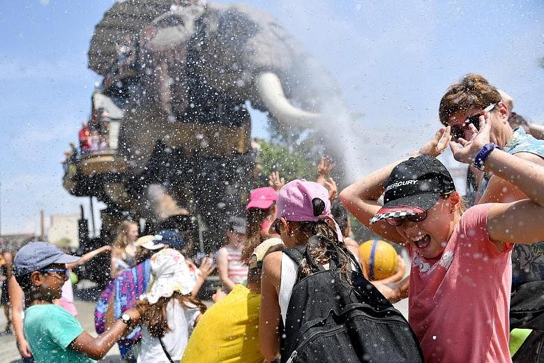 Children enjoying cool relief from water sprayed by a mechanical elephant at the Machines of the Isle of Nantes project in France. In Europe, temperatures of around 40 deg C have contributed to a wildfire in Portugal over the weekend, killing 64 peop