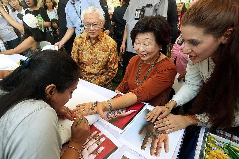 President Tony Tan Keng Yam's wife, Mary, having her hand painted with henna during the Istana Open House yesterday. Earlier, the President and his wife caught a performance by the Yishun Secondary School symphonic band. Despite some wet weather earl