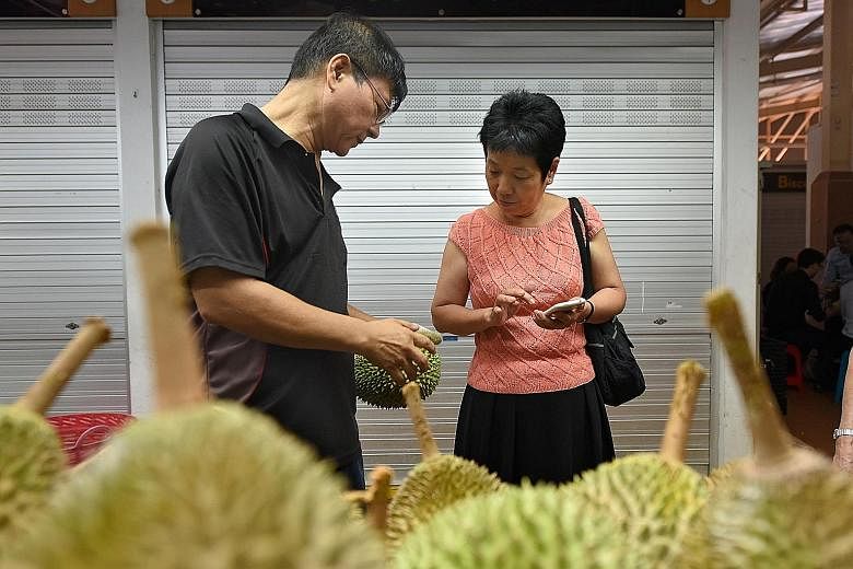 Mr Steven Shui Poh Sing, owner of Ah Seng Durian at Ghim Moh Market, cracking open a durian for a customer. Durian vendors said business may pick up in the coming weeks - prices are expected to fall slightly as the current season approaches its peak.
