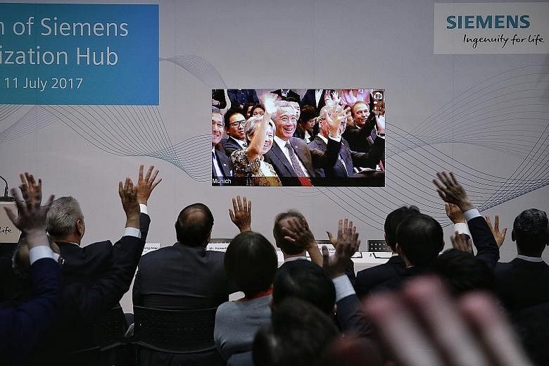 Prime Minister Lee Hsien Loong and Mrs Lee waving over a live video feed from Munich to Minister for Trade and Industry (Industry) S. Iswaran (second from left) and Siemens representatives in Singapore yesterday. PM Lee opened the Siemens Digitalisat