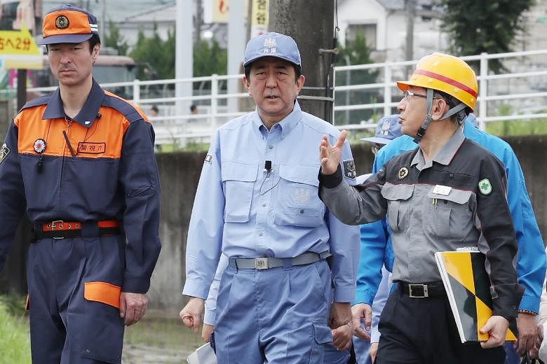 Japanese Prime Minister Shinzo Abe (centre) inspecting a flood-affected area in Hita, Oita prefecture, yesterday. The death toll from heavy rain and flooding in Japan's south has risen to 25. Mr Abe has promised help to rebuild the devastated region.