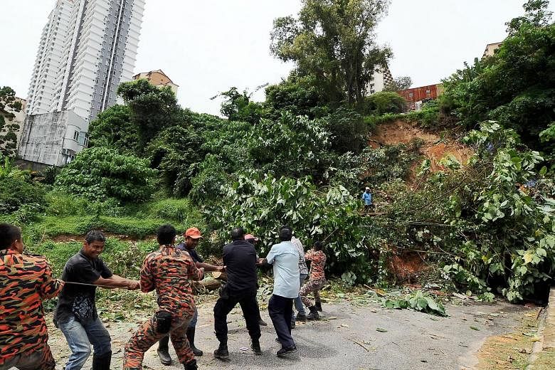 Firemen helping to clear a fallen tree after a landslide yesterday morning in George Town, Penang.