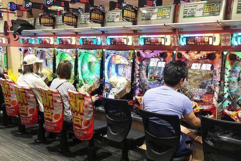 Top: A long queue forms outside a pachinko parlour near a train station in Tokyo before its doors even open one morning in May. Above: Pachinko machines are easy to play, readily available and cheap, drawing in an array of Japanese people from commut
