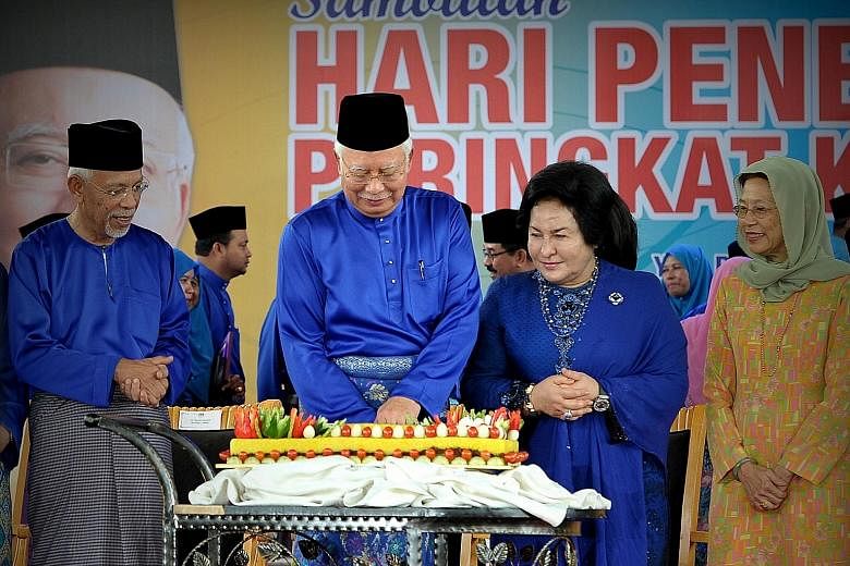 Above: Mr Najib Razak and his wife, Datin Seri Rosmah Mansor, with a traditional pulut kuning (Malay glutinous rice) cake at the Felda event in Putrajaya. He later cut the cake to celebrate his 64th birthday. Right: Felda landowners cheering the anno