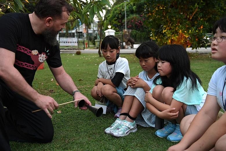 Children from the Japanese town of Hirono - (from left) Yumi Koretsugu, Kotoha Watanabe, Saito Rin and Sayo Ochiai, all 10 - listen as instructor Desmond Hinkson demonstrates the agogo, an instrument used in the Brazilian martial art capoeira, which 