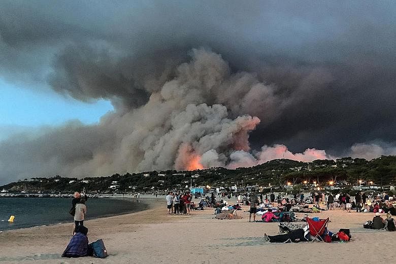 People finding refuge on a beach as fire burns a forest in the coastal village of Bormes-les-Mimosas, France, at sunrise yesterday. About 3,000 of those evacuated were tourists.