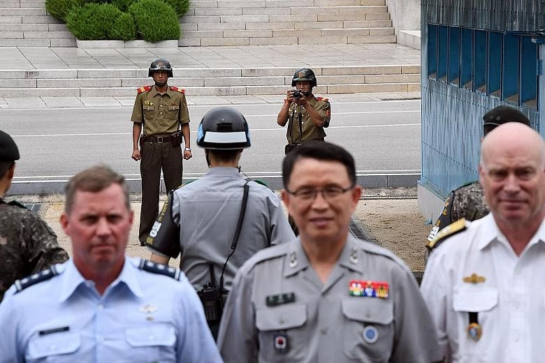 North Korean soldiers (in background) watch as senior members of the United Nations Command (in foreground) pose for a photo on the South side after attending a commemorative ceremony for the 64th anniversary of the Korean armistice at the truce vill