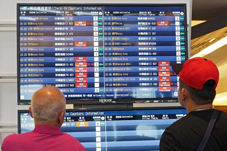 Passengers checking flight information at Taoyuan International Airport yesterday. Many flights were delayed or cancelled as Typhoon Nesat approached Taiwan. Strong winds blew over people and motorbikes in Taipei yesterday as Typhoon Nesat neared. Se