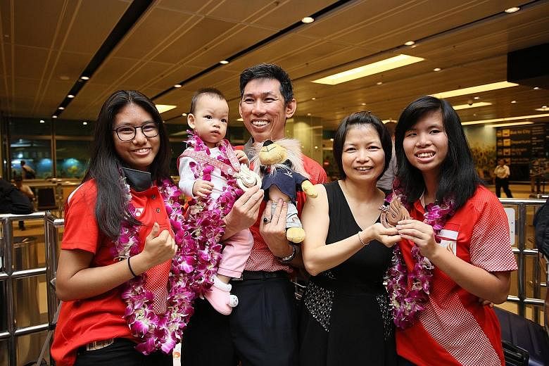 Gold medallist Adelia Naomi Yokoyama (left) and bronze medallist Kimberly Quek (right) pose for a photo with their coach Liew Foo Wai and his family after arriving at Changi Airport yesterday. National bowlers Yokoyama and Quek, who won Singapore's f
