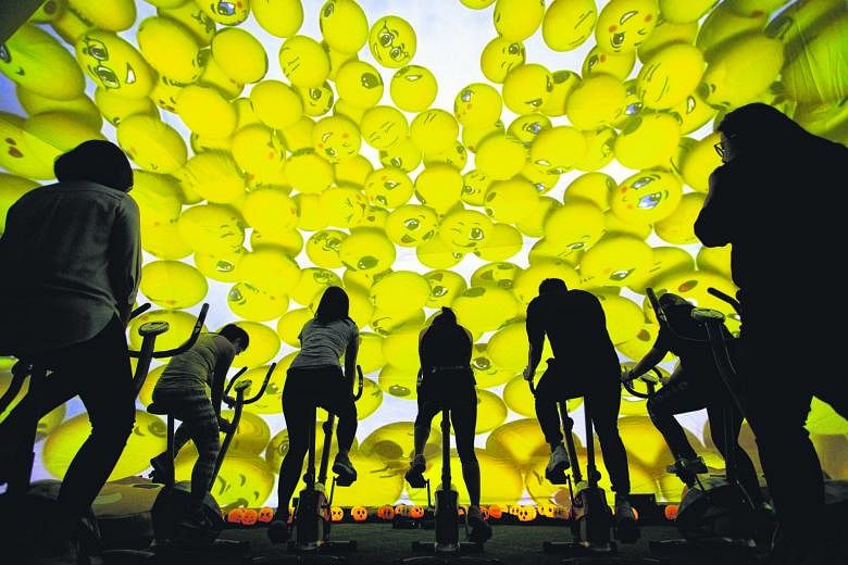 Cyclists on stationary bikes at Raffles City during CapitaLand Malls' Cyclo-moji-rama event yesterday. Featuring a 10m dome adorned with beaming emoji, participants cycled with the aid of a panoramic display that changed scenery as they pedalled. Cap