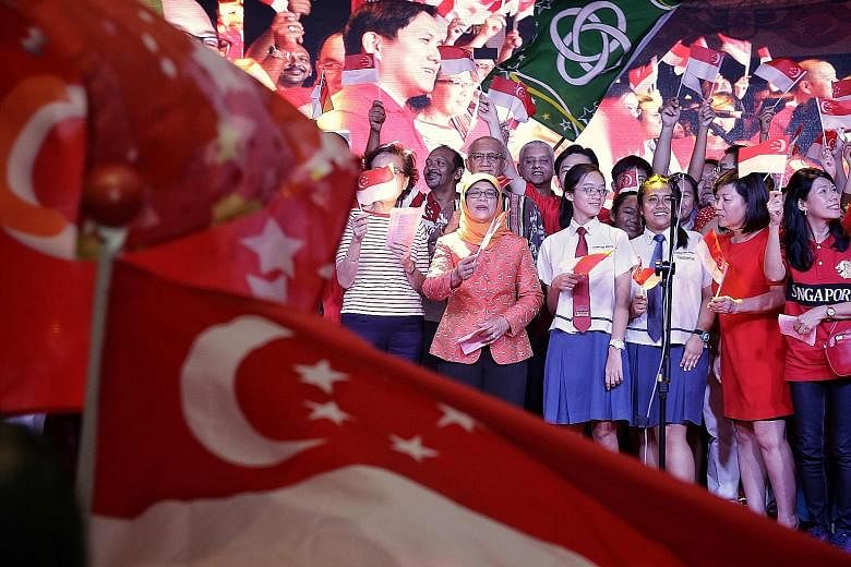 Madam Halimah Yacob, with her husband Mohammed Abdullah Alhabshee behind her, joining in a mass singing of National Day songs at the Marsiling National Day dinner celebration on Sunday.